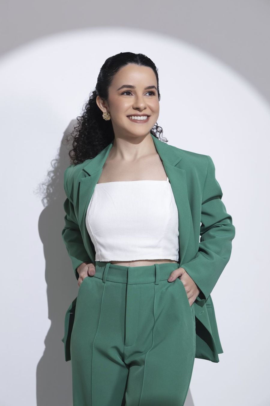 Dra. Larissa Quariguasi em pé, sorrindo, com as mãos nos bolsos