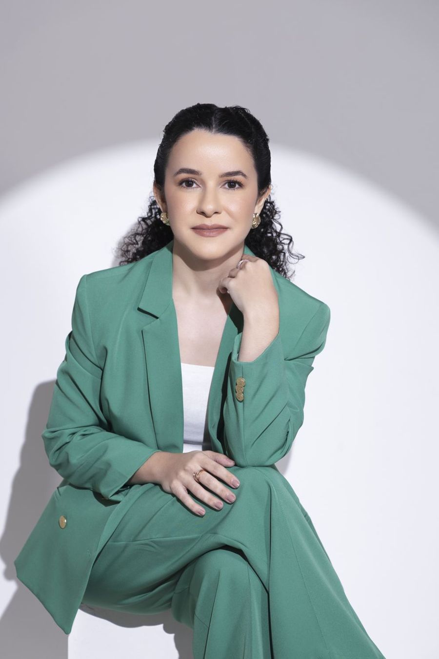 Dra. Larissa Quariguasi, de blazer verde, sentada e olhando para a câmera